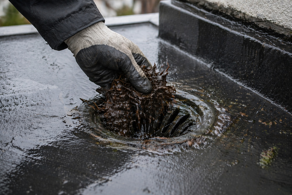 Flat roof drainage outlet being cleared to prevent leaks in Bristol